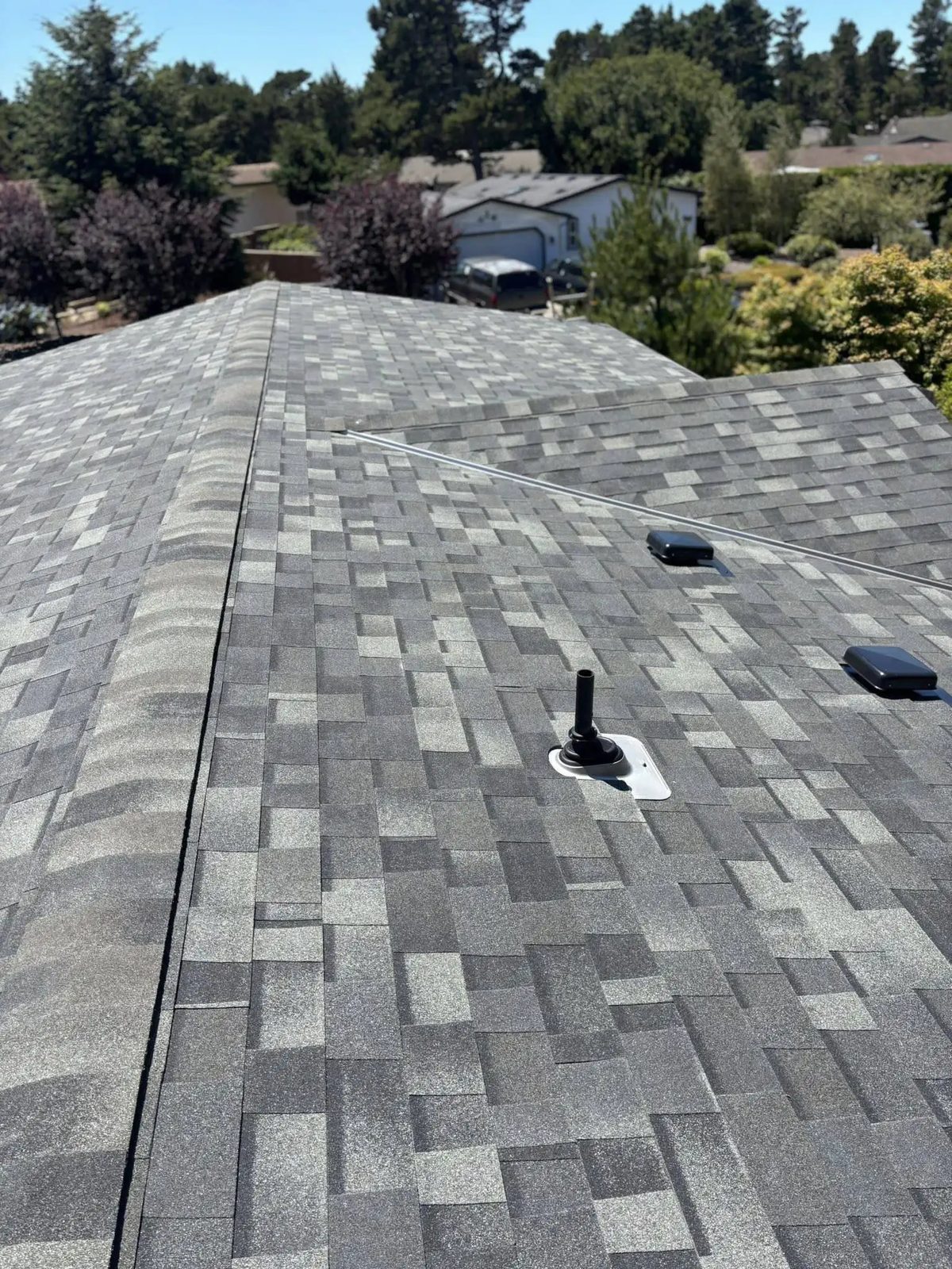 A finished Pacific Peaks shingle roof on a coastal Oregon home, with the neighborhood beyond